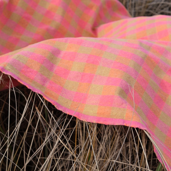 Pink and green checkered blanket draped over dry grass. laid towel with tassels. Checker Gingham Picnic Blanket.