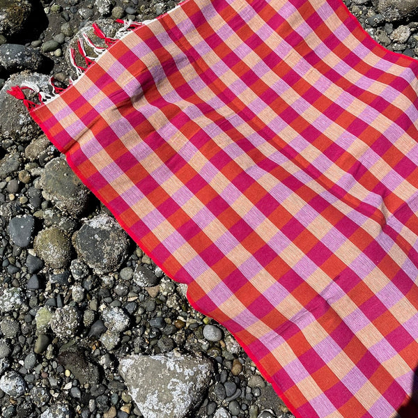 Plaid towel with tassels on a textured surface.  Checker Gingham Picnic Blanket.