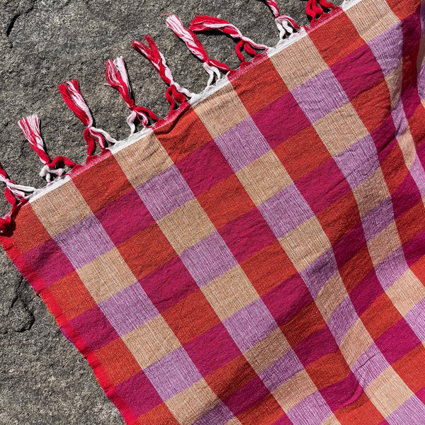 Plaid towel with tassels on a textured surface.  Checker Gingham Picnic Blanket.